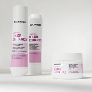 Goldwell Dualsenses Color Extra Rich haircare products shown as shampoo, conditioner and treatment jar in white and pink packaging on a soft light grey studio background.