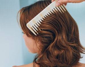 Goldwell Dualsenses Color Extra Rich image showing a comb running through wavy auburn hair in a soft blue studio setting.