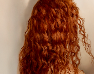 Goldwell Dualsenses Curls & Waves image showing a person from behind with long curly red hair against a neutral studio background.