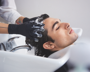 A man rests his head back into a hair salon basin as his stylist uses Goldwell's Dualsenses Men's range products to clean and revitalize his look