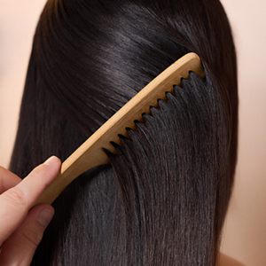Goldwell Dualsenses Pure Hydration product held beside a person’s long dark hair on a soft blue studio background.