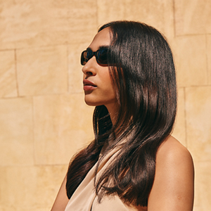 A model stands enjoying the sunshine in dark sunglasses knowing her hair is protected from damage by Goldwell's Dualsenses Sun Reflects range