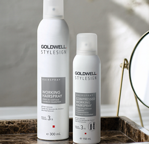 A shot of Goldwell's StyleSign Working Hairspray (300ml) and Compressed Working Hairspray (150ml) in a shallow brown marble dish in front of a small, round tabletop mirror