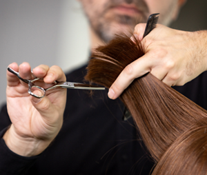 A Goldwell Master Stylist uses one hand to hold a section of hair as he trims the end with hairdresser's scissors