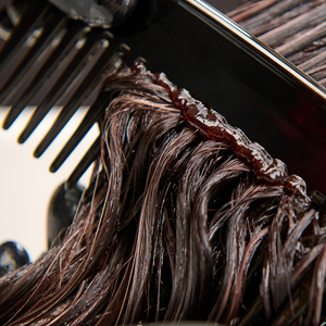 Goldwell Elumen collage extra small image showing a close-up of dark hair coated with color as a comb separates the strands during salon application. 