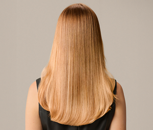 Goldwell Elumen Color transformation after image showing the back of a model with smooth, glossy, warm blonde hair against a neutral beige background.