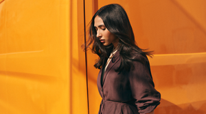 In front of a bright orange backdrop, a model shows of the sleek shine of her flowing dark hair, created thanks to Goldwell's range of products.