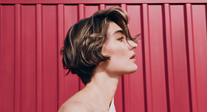 Goldwell Elumen hero banner featuring a model with short textured hair in white top against red paneled background