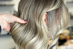 Stylist examining ash blonde hair with lowlights and babylights