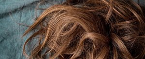 Close-up of dry, distressed brunette hair against a green background