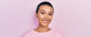 Smiling woman with short hair standing against a pink background