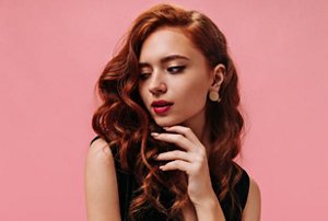 Woman with light red cherry cola hair colour against a pink background