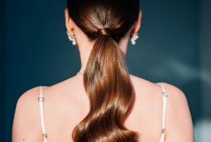 Woman with auburn hair styled in a long, glossy ponytail
