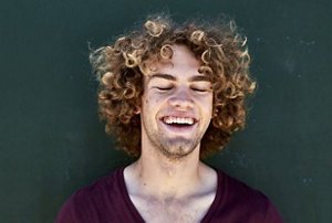 Laughing man wearing a maroon top with naturally curly hair