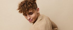 Smiling young man in a tan jumper with coily, corkscrew curls