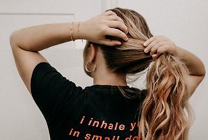 Woman with long wavy hair tying her hair back into a ponytail