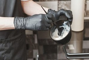 Hairdresser wearing latext gloves and mixing bleach in a black pot