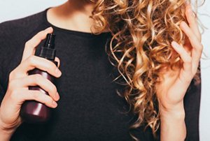 Woman with dark golden blonde hair using a dry shampoo spray