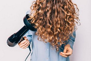 Woman using her hairdryer's diffuser to dry her natural curly hair