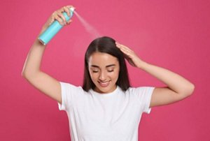Woman spritzing dry shampoo on her hair to get the fluffy hair look