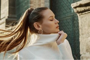 Woman wearing a long white jumper with a slicked-back ponytail
