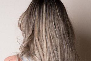 Woman with light greige hair with a dark blended root smudge