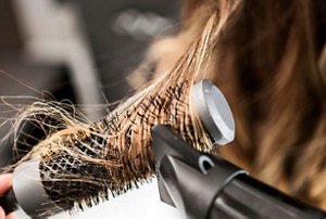 Close-up of a woman styling her hair with a rounded brush and a hairdryer