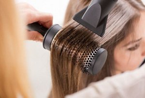Woman having her long hair styled with a hairdryer and a rounded brush
