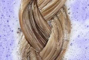 Plaited blonde hair soaking in a foamy mix of water and purple shampoo