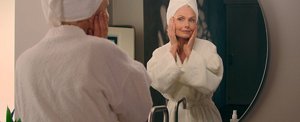 Menopausal woman wearing a dressing gown applying a face serum after showering