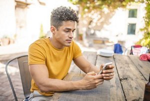 Man with a taper fade haircut texting at an outdoor cafe table