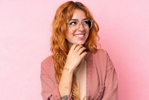 Woman with dyed red hair standing against a pink background