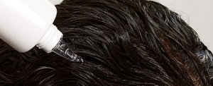 Close-up of a woman applying a scalp serum to her thick, dark hair