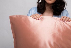 Woman with dark hair holding on to a pink satin pillowcase