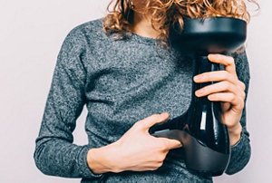 Woman wearing a grey top drying her curls with a diffuser attachment