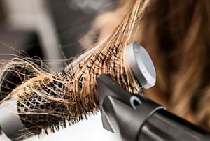 Close-up picture of a woman heat styling her hair with a rounded brush