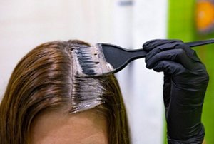 Stylist applying a beige-blonde tint to a client's roots