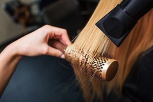 Woman with dark blonde hair having her hair styled with a rounded brush and a hairdryer