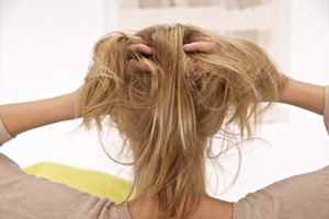 Back of a blonde woman's head. She's massaging her scalp.