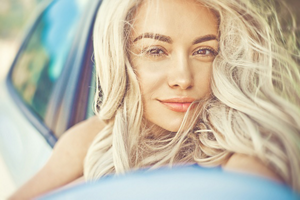woman with bleached blonde wavy hair looking at camera sat in a car