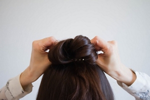 Brunette woman securing her hair into a bun