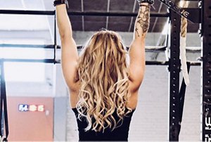 Blonde woman with balayaged curly hair using gym equipment