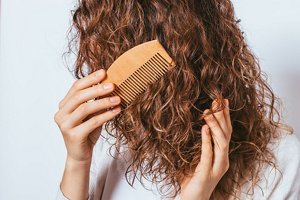 Woman gently running a wooden comb through damp curly hair