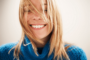 close up image of woman with blonde highlighted hair and a blue jumper, with her eyes shut and smiling