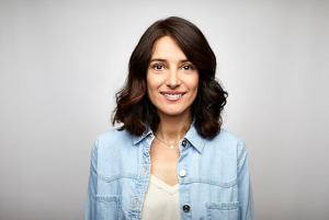 smiling woman with shoulder length brown wavy hair wearing a denim shirt