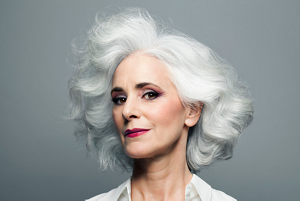 Glamorous older woman with short curly grey hair looking at the camera and wearing a white shirt
