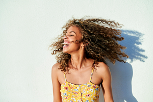 woman with brown curly hair laughing wearing a yellow floral dress