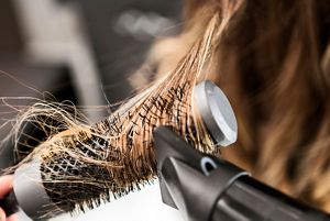 Brunette woman using a curling brush and hairdryer