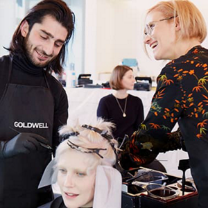 Two smiling hair stylists styling a blond woman